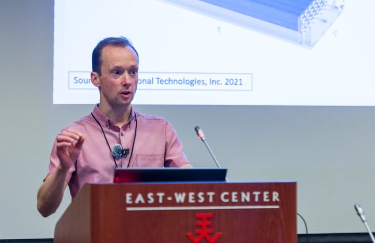 Dr Michael Aspinall stood behind a lectern giving a presentation at the Haleakalā Neutron Monitor Workshop and Ribbon Cutting Ceremony, Hawaii, 5-9 Jan 2025. Presentation titles given: System overview and design justifications for the United Kingdom’s new neutron monitor, the NM-2023; and Monte Carlo design optimisation for the United Kingdom’s new neutron monitor, the NM-2023. Dr Michael Aspinall stood behind a lectern giving a presentation at the Haleakalā Neutron Monitor Workshop, Hawaii.